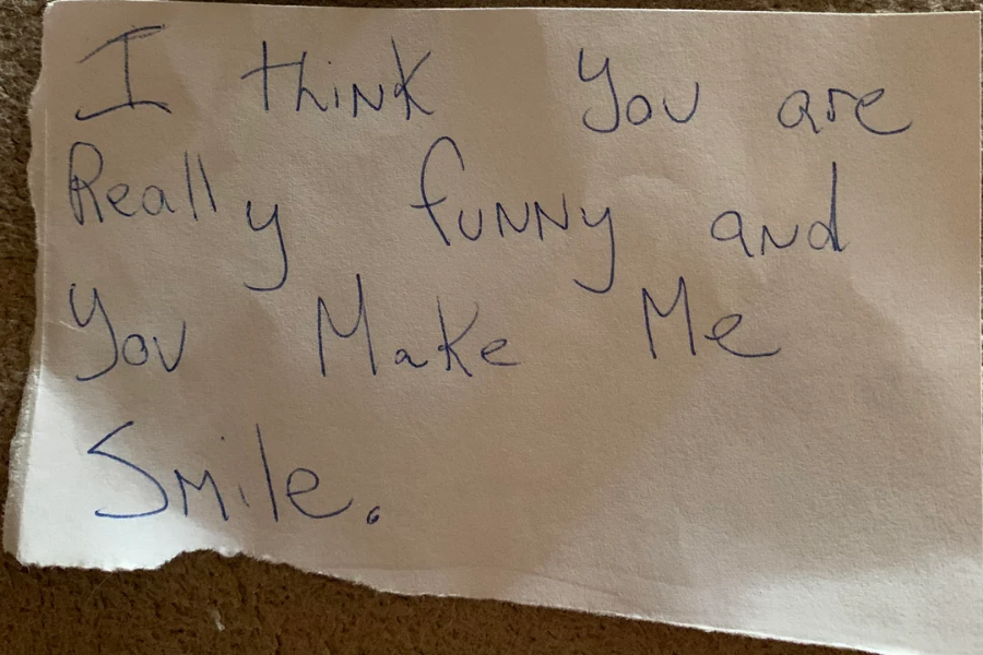 A handwritten note on torn white paper reads, "I think you are really funny and you make me smile." The message is written in blue ink with a mix of cursive and print-style lettering.