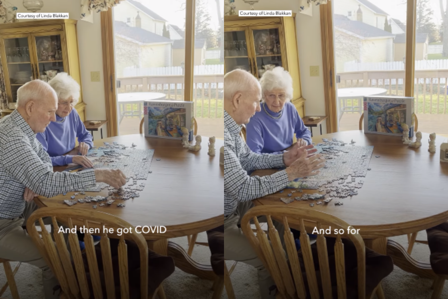 A split image shows an elderly couple sitting at a round wooden dining table, working on a large jigsaw puzzle together. The man wears a plaid shirt and the woman wears a light purple top, both engaged and smiling. A puzzle box with artwork labeled “Ravensburger” is visible in the background, along with subtitle text reading “And then he got COVID” and “And so for.”