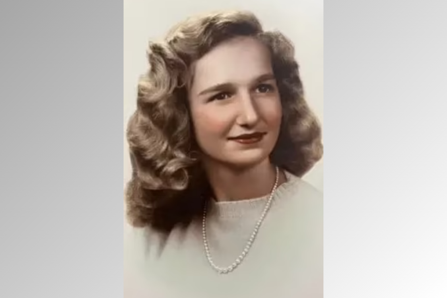 A hand-colored vintage portrait of a young woman with softly curled blonde hair, wearing a light sweater and a single-strand pearl necklace. She gazes slightly off-camera with a calm expression against a pale gradient background.
