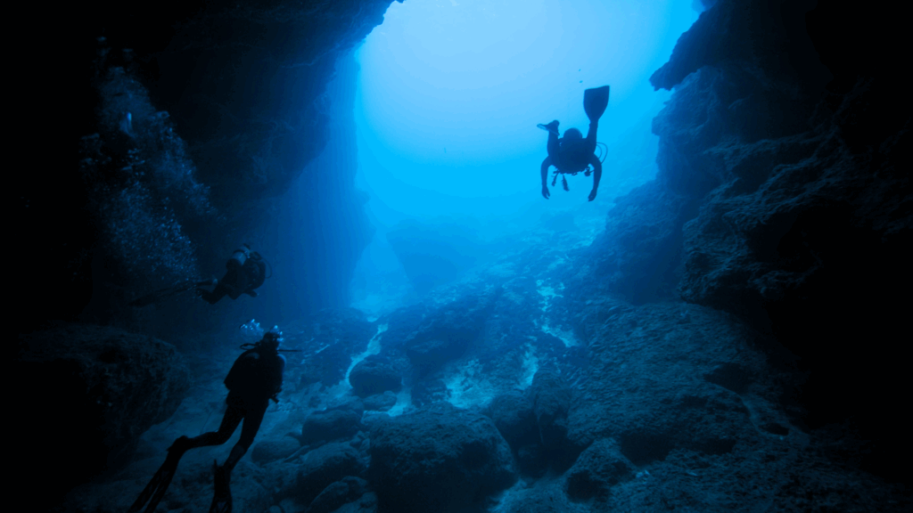 Divers exploring a large underwater cave with flashlights