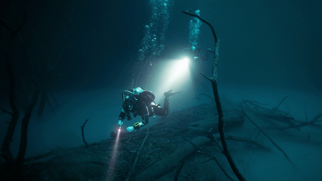 Scuba diver in dark water holding flashlight underwater