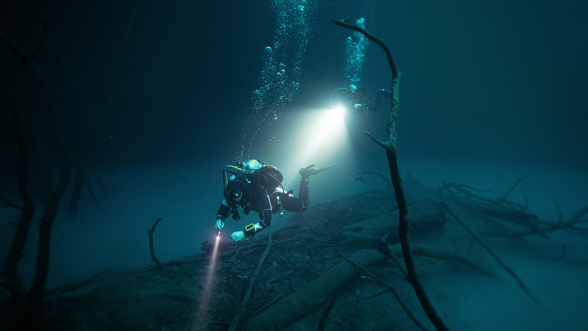 Scuba diver in dark water holding flashlight underwater