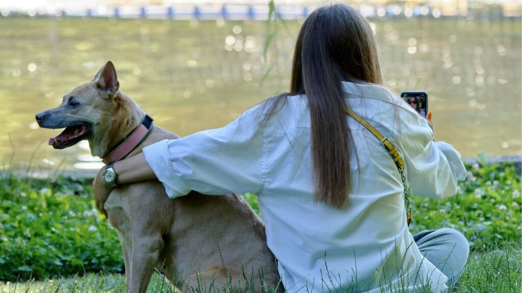 A woman holding her dog by a lake