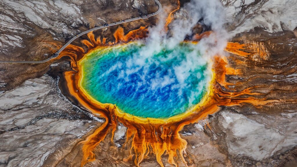 An aerial view of the Grand Prismatic Spring in Yellowstone shows vivid blue water surrounded by rings of green, yellow, and orange bacteria mats.