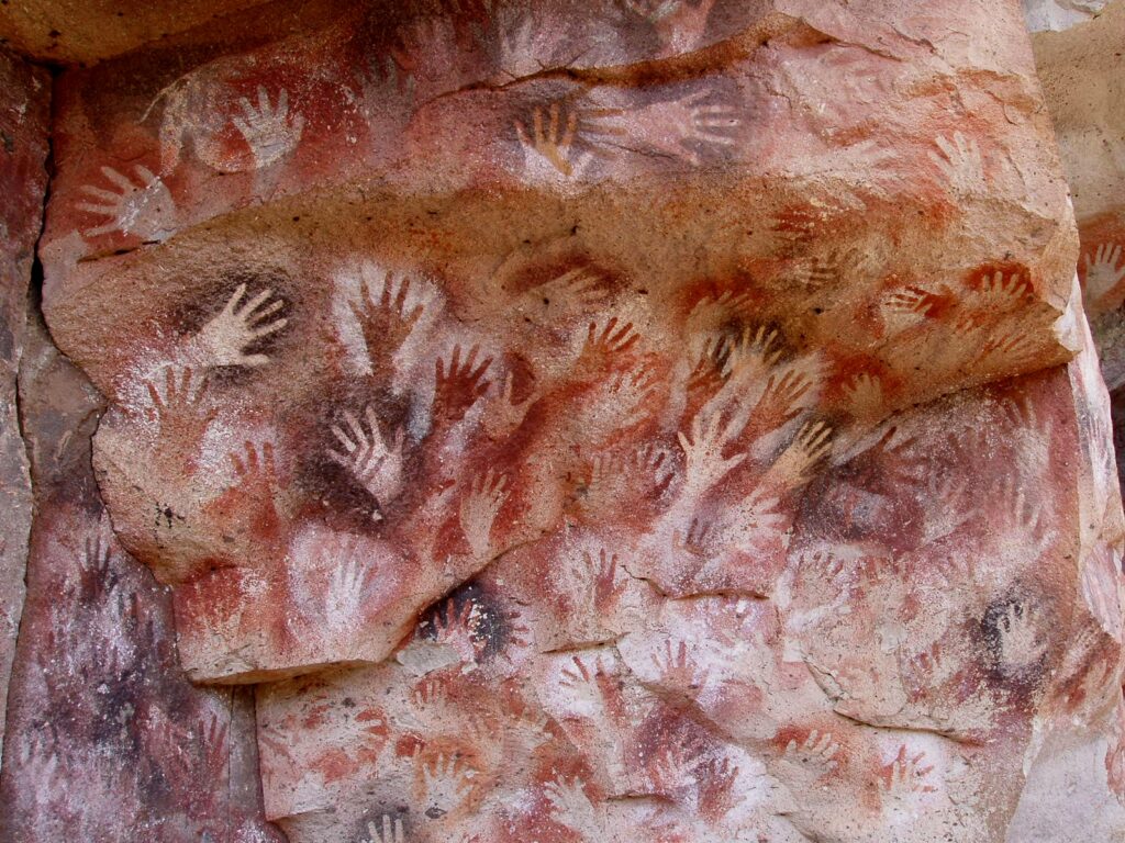 Ancient handprints painted on a cave wall in red, white, and black pigments.