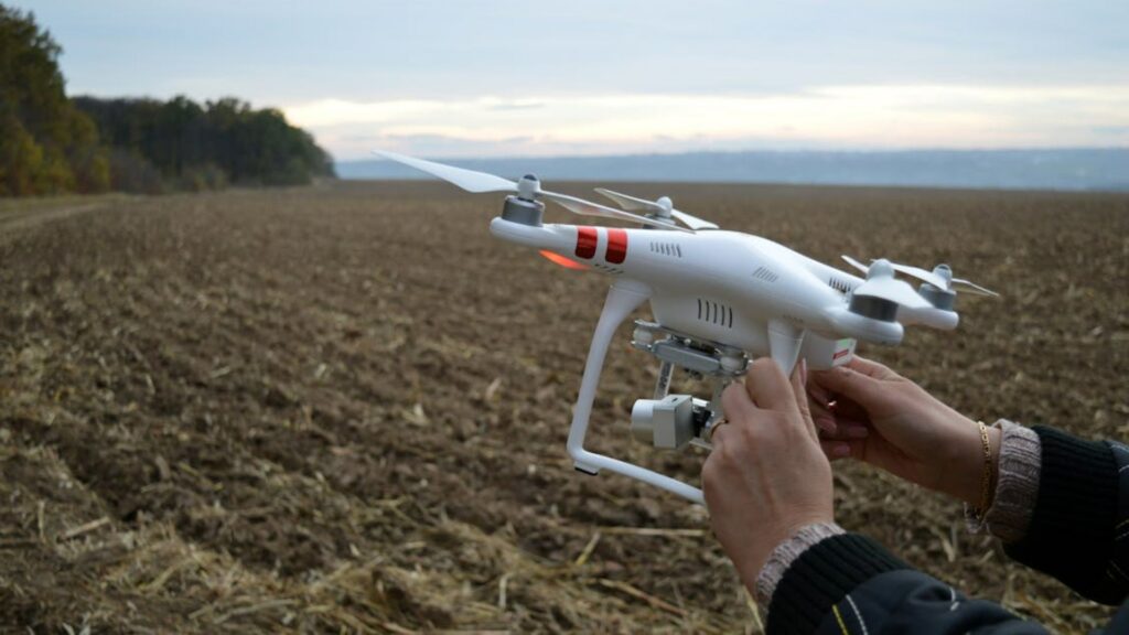 Person holding a drone over a wide open plowed field about to use it.