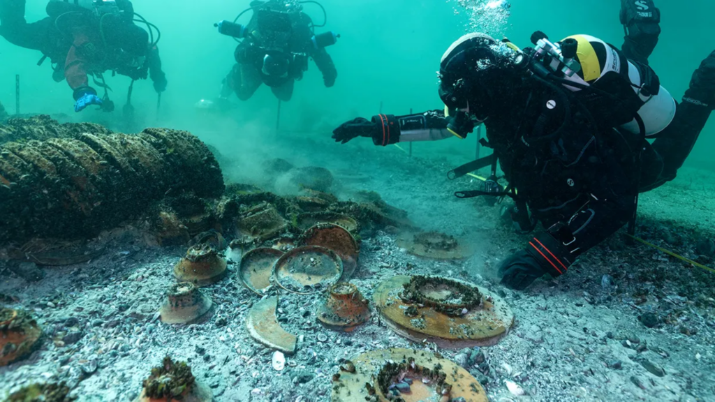 Three scuba divers explore old broken pottery scattered on the ocean floor.