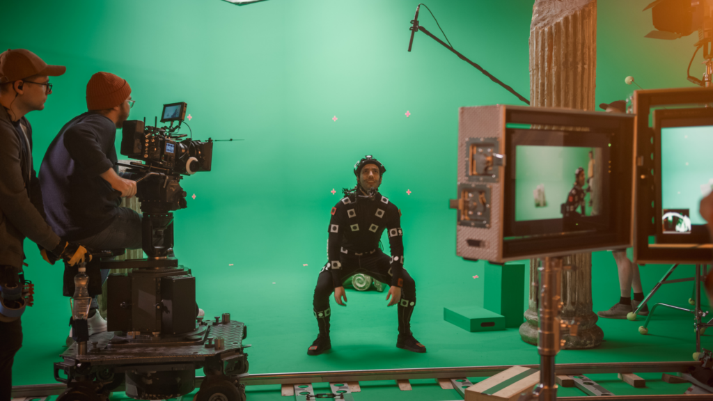 A camera operator films an actor wearing a motion-capture suit in front of a green screen.